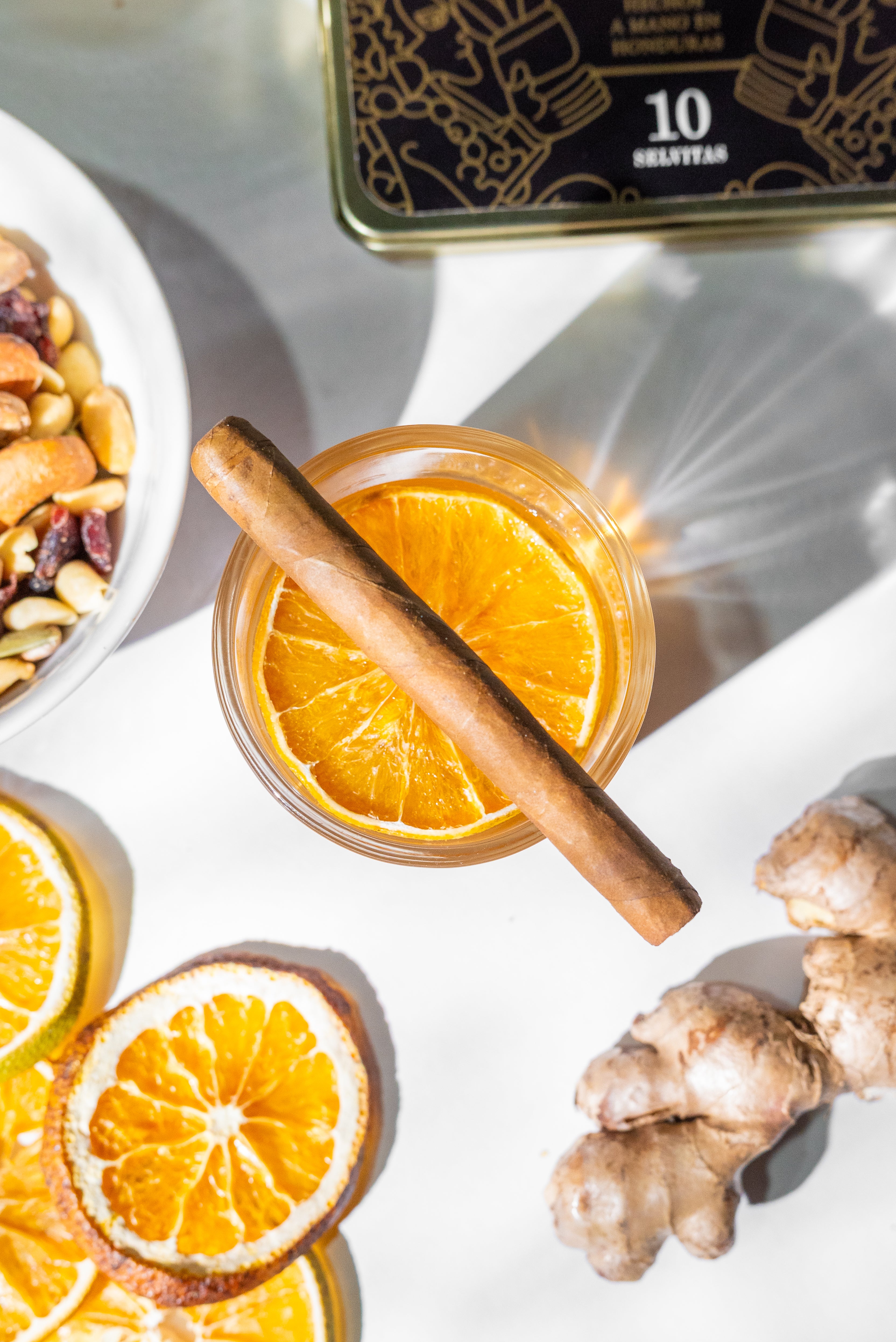 Selvita Zigarillo mit Asche auf Orangencocktail, Nüsse und Zitrus rundherum