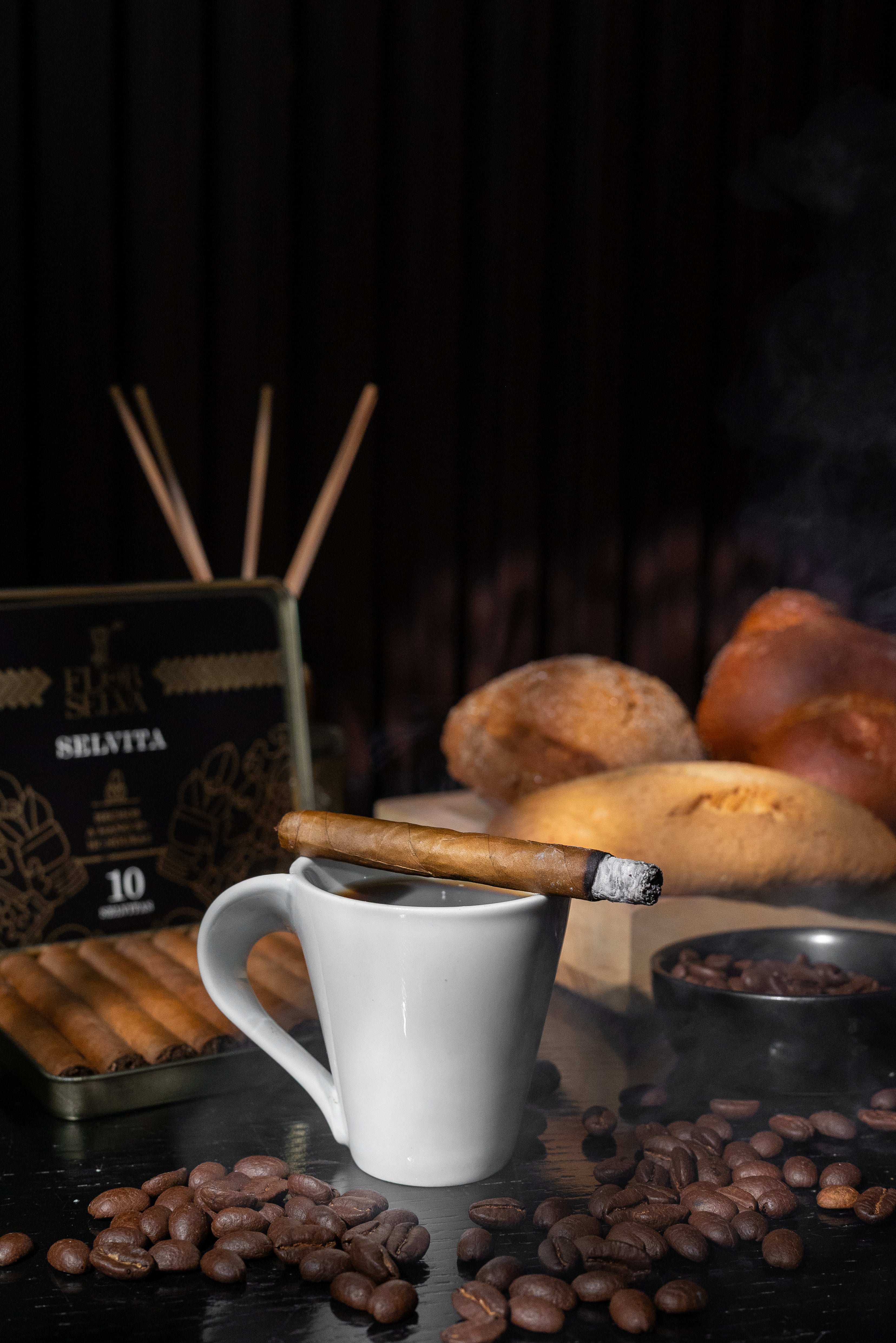 Selvita Zigarillo auf Kaffeetasse, umgeben von Bohnen und Brot im Hintergrund