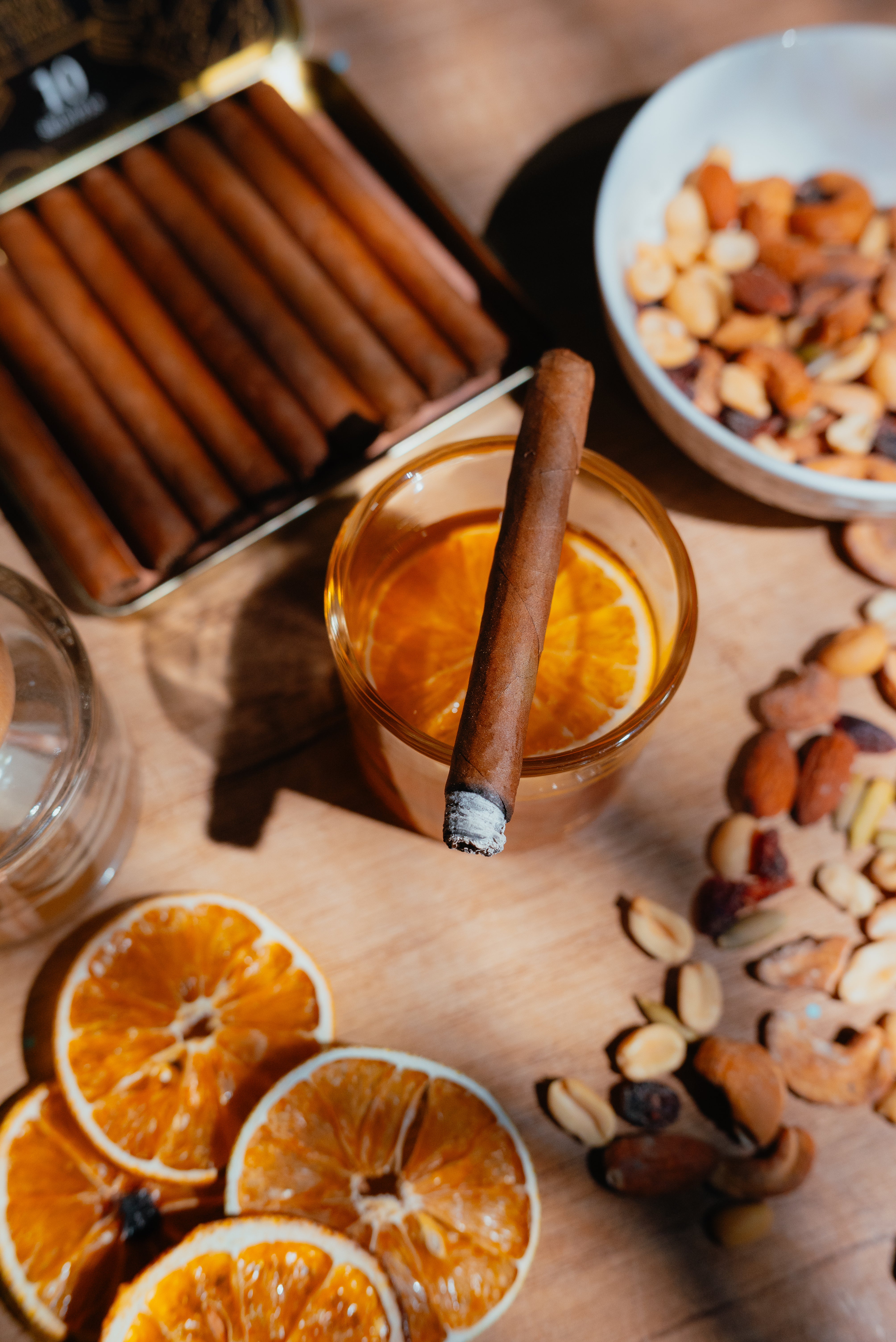 Zigarillo auf Glas mit Orangenscheibe, Ingwer und Nüsse auf hellem Tisch