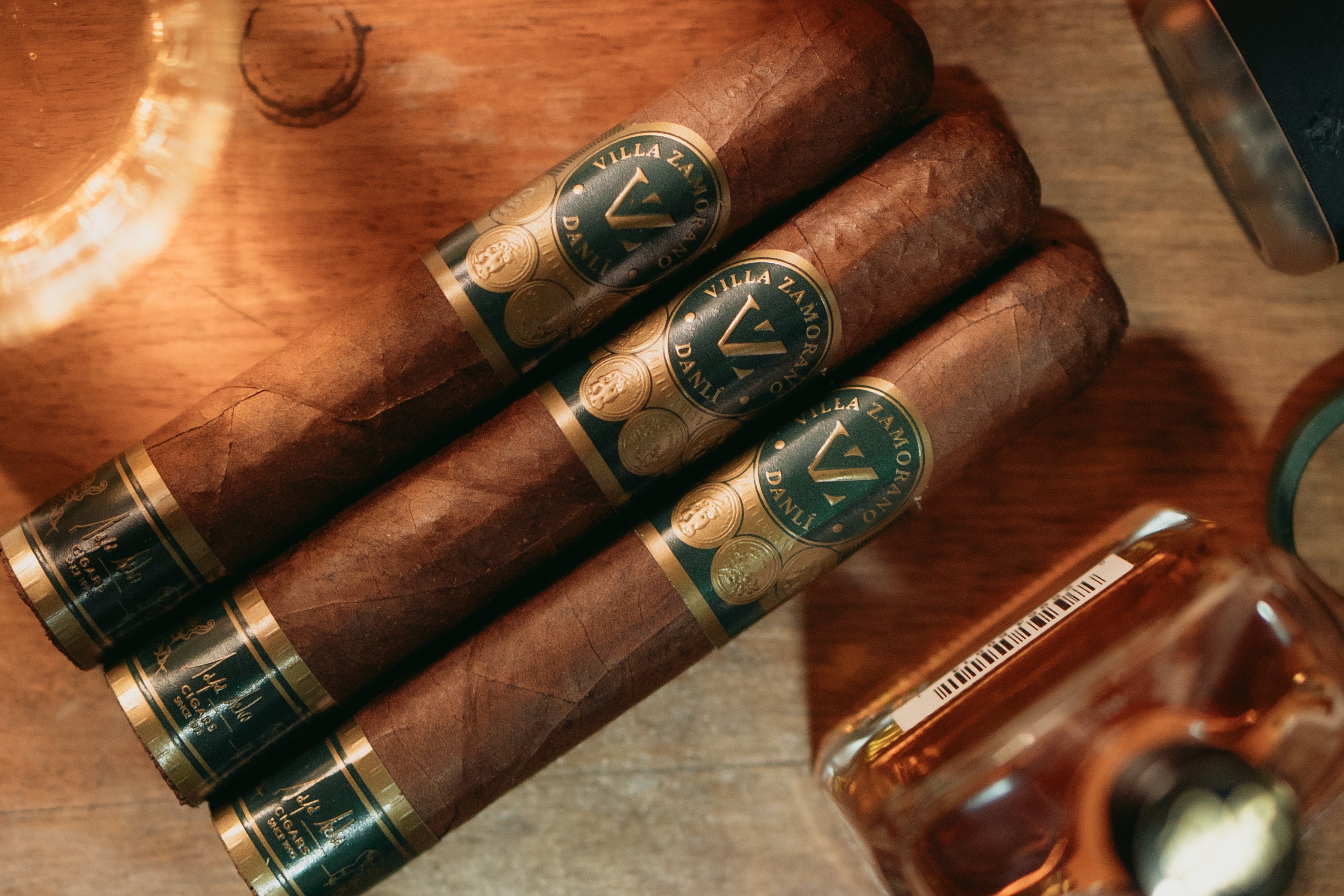 Drei Villa Zamorano Danlí Robusto Zigarren auf Holz mit Glas und Rum