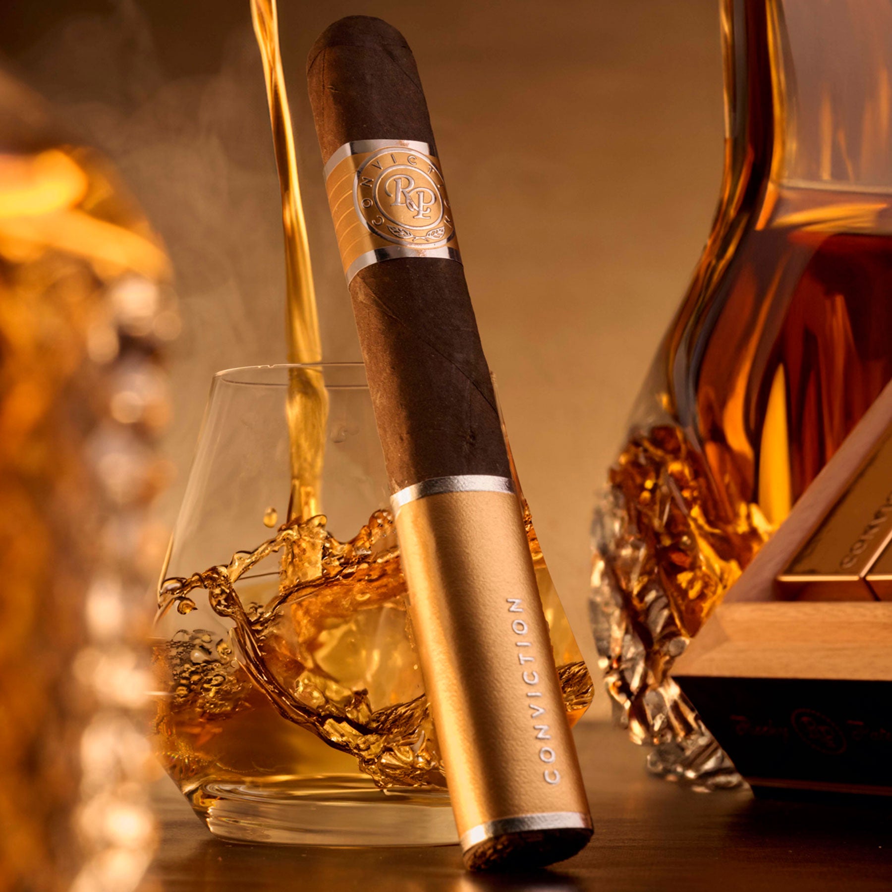Rocky Patel Conviction Toro Zigarre in goldener Tube vor Whisky-Glas und Karaffe